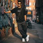 Man wearing a black CODE92 oversized organic cotton t-shirt with cargo pants and white sneakers in an urban alleyway.