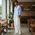 CODE92 sky blue linen shirt with white front panel detail worn by a man in a cafe setting with white trousers