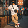 A man wearing a CODE92 white oversized organic cotton t-shirt with khaki cargo pants and a black crossbody bag.